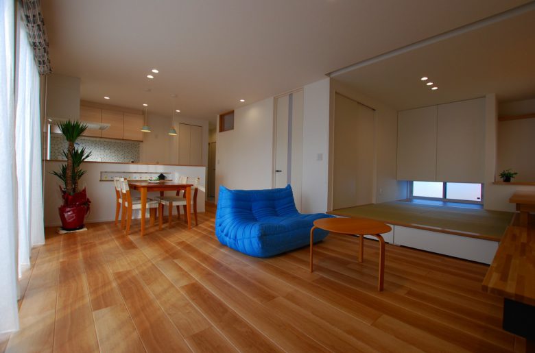 入口のHiドアで部屋に広がりをもたせ、南側の大きな窓から光をとりこむことで、明るいリビングが実現。小上がりの畳スペースの下には引き出し式の収納を確保。